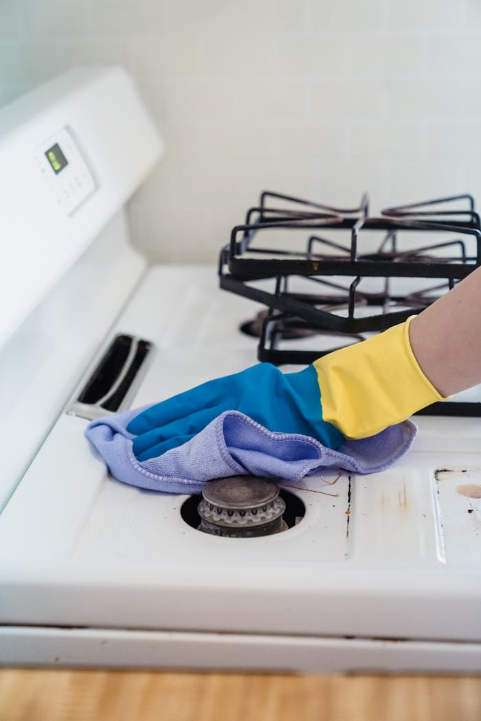 about-02 A close-up of a hand in gloves cleaning a gas stove with a cloth.