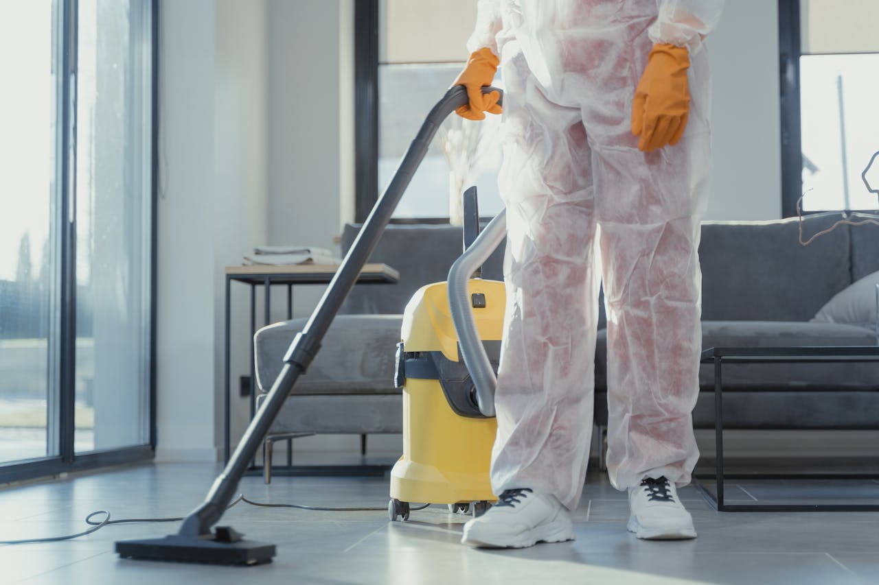 hero-02 A cleaner in protective coveralls and gloves vacuuming a modern living room.